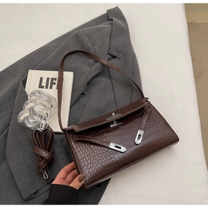 Detail view of dark brown crocodile-embossed handbag with silver twist lock and strap