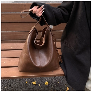 Detail of dark brown tote bag on wooden bench with autumn leaves showing leather texture