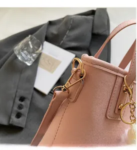 Detail of pink suede bucket bag with gold metal hooks and white pom-pom charm