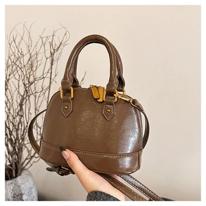 Detail of dark brown crinkled patent leather shell bag with gold hardware and top handle