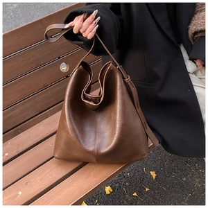 Detail of deep brown textured leather tote bag with vertical stitching on wooden bench