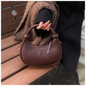 Close-up of a dark brown half-moon handbag with knot detail and golden zipper on a wooden bench