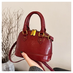 Detail view of a dark red glossy shell bag with golden zippers and a detachable shoulder strap