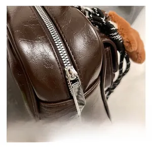 Detailed macro view of dark brown glossy PU leather bag with silver zipper and plush bear charm