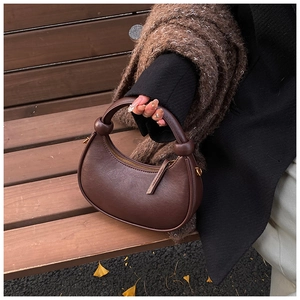 Detail of dark brown leather half-moon bag with knot handle design on a wooden bench