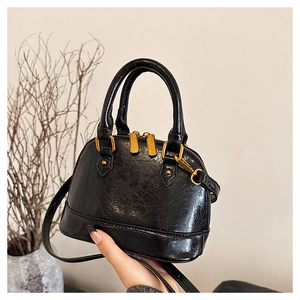 Detail of black glossy patent leather shell bag with gold hardware and top handle