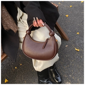 Detail of dark brown crescent bag featuring minimalist knot handle and zipper closure