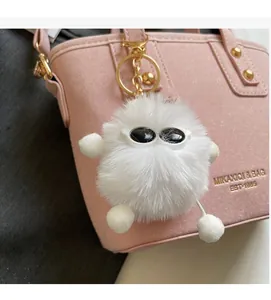 Close-up of a white plush monster keychain with sunglasses on a pink leather handbag