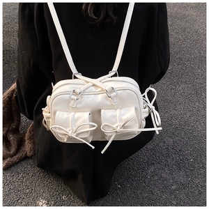Detail of a creamy white Boston bag with bow accents worn by a model in a black coat