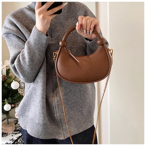 Close-up of brown leather crescent bag featuring a round handle and gold chain strap