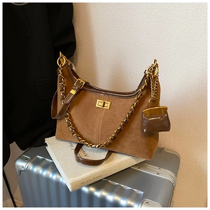 Detail der braunen Wildledertasche mit goldener Kette und Mini-Taschenanhänger auf Koffer