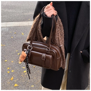 Detail of dark brown vintage Boston bag with plush bear charm held by model outdoors