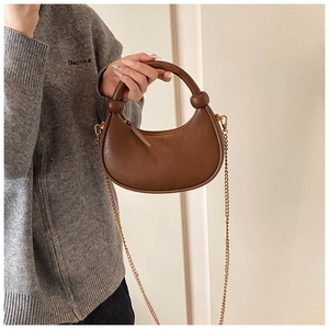 Detail of brown half-moon crossbody bag with gold chain strap and chunky handle