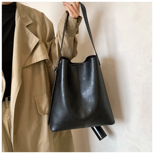 Minimalist black faux leather tote bag with vertical seam detail shown on shoulder