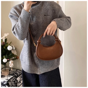 Close-up of brown crescent leather bag with knotted handle and gold chain strap