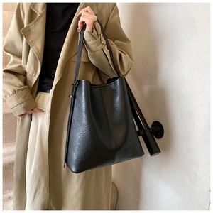 Minimalist black leather tote bag worn with a khaki trench coat for a casual street style