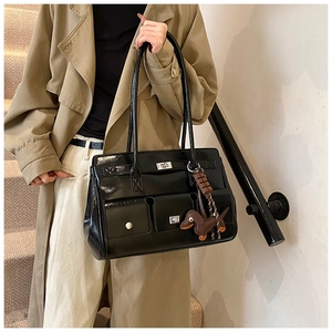 Close-up of black glossy patent leather shoulder bag with pockets and dachshund charm