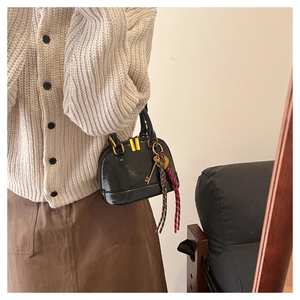 Close-up of black patent leather mini bag with gold zipper and woven rope detail