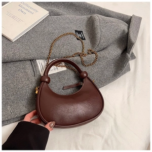 Close-up of dark brown crescent bag featuring gold chain and spherical knot detail