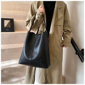 Close-up of black textured leather tote bag worn on shoulder in a stylish staircase setting