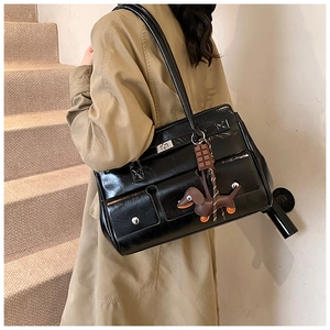 Detail of black patent leather shoulder bag with rotating lock and cute dog charm
