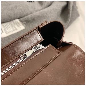 Close-up of smooth silver metal zipper and stitching detail on brown leather bag