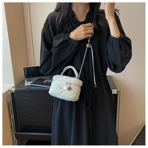Detail of white quilted crossbody bag with silver chain and camellia flower charm