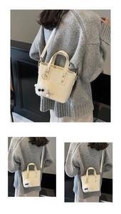 Detail of a beige bucket bag with plush charm and detachable strap on a grey sweater