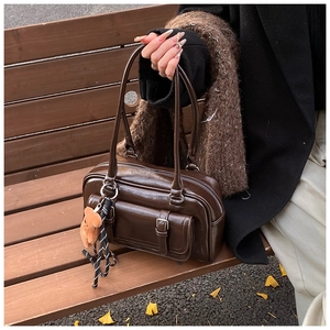 Close-up of a vintage brown PU leather Boston bag on a wooden bench with bear charm