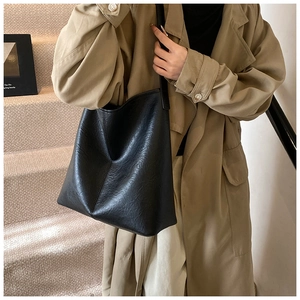 Detail of minimalist black tote bag with leather texture worn with a beige trench coat