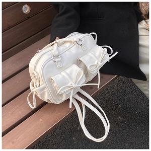 Detail shot of off-white bow handbag with silver zippers on a wooden bench