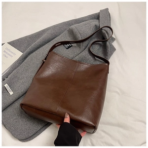 Detail of minimalist dark brown leather tote bag with vertical stitching on wool coat