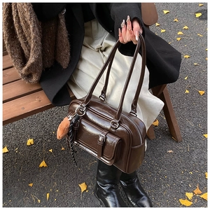 Detail of a dark brown glossy leather Boston bag featuring a furry charm and metal buckle