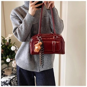 Deep red leather Boston bag with teddy bear charm and striped tassel in a winter setting