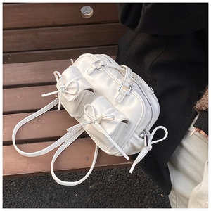 Detail view of white Boston bag with bow accents and silver metal buckles on a bench