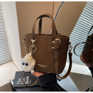Detail of brown felt bucket bag with white branding text and a plush monster charm