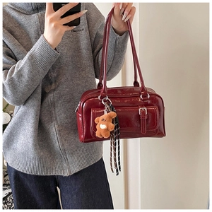 Detail of burgundy patent leather bag with brown plush bear charm and glossy finish