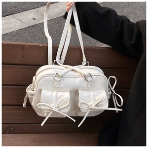 Close-up of cream Boston bag with decorative bows and 3D pockets on a wooden bench