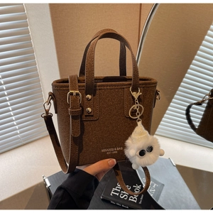 Detail of dark brown felt bucket bag featuring gold lettering and soft white fur charm