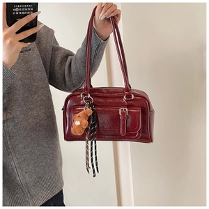 Detail of dark red patent leather shoulder bag with bear pendant and striped ribbon