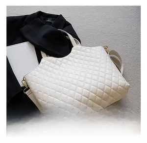 Detail view of white quilted tote bag featuring golden hooks and wide shoulder strap