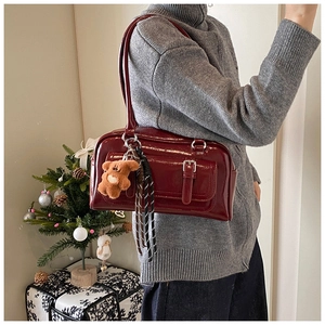 Detail of burgundy glossy leather shoulder bag with plush bear charm and buckle pocket