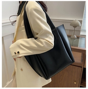 Dettaglio di una grande borsa tote in pelle nera con tasca frontale portata a spalla