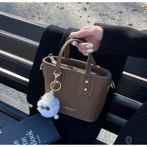 Brown wool bucket bag with gold hardware and plush monster charm on a winter bench