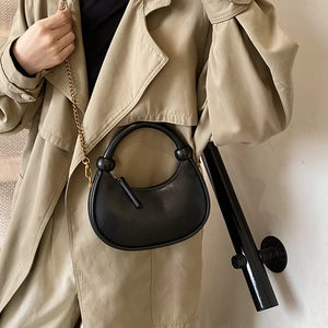 Minimalist black crescent shoulder bag with gold chain strap shown on a beige coat