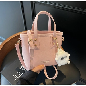 Detail of pink faux suede bucket bag with branding and a white fuzzy monster charm