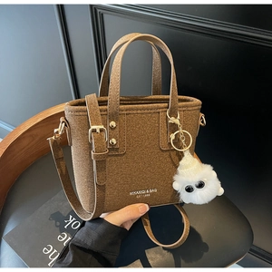 Detail of a brown felt bucket bag with white logo lettering and a plush monster charm