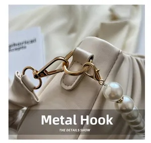 Close-up of golden hardware hook and elegant white pearl strap on beige leather bag