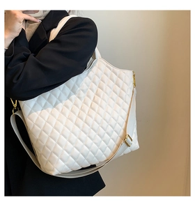 Detailed view of white quilted tote bag with wide strap and gold hardware on model