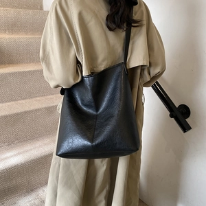 Minimalist black faux leather large tote bag shown in a shoulder carry position